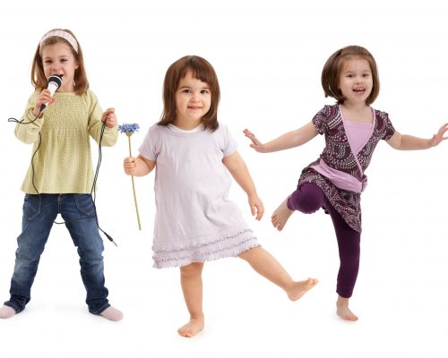 Three cute little girls dancing, singing to microphone, having fun over white background.