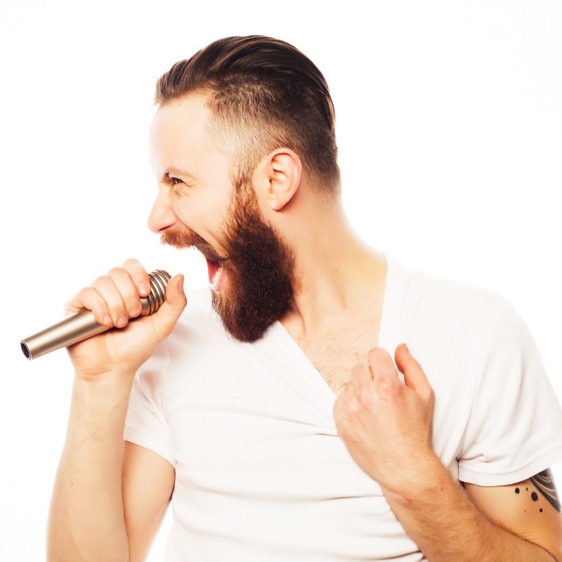 man with microphone Life style concept: a young man with a beard wearing a white shirt holding a microphone and singing.Isolated on white.