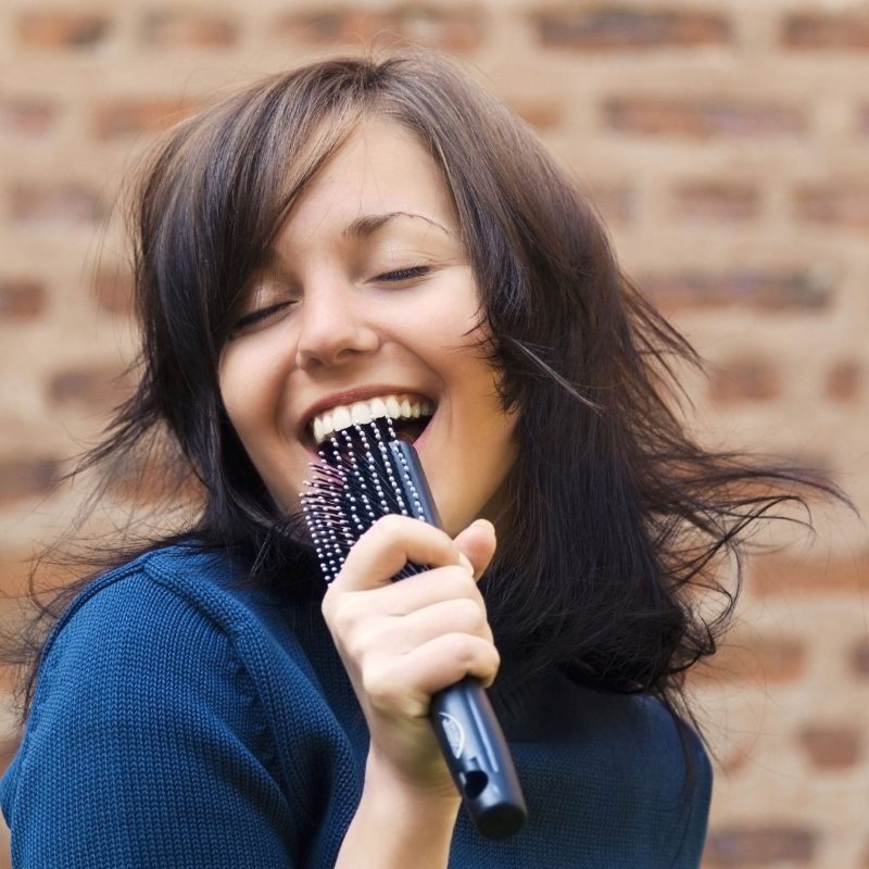 Young tousle-headed brunette pretending to sing with her hair brush as a microphone